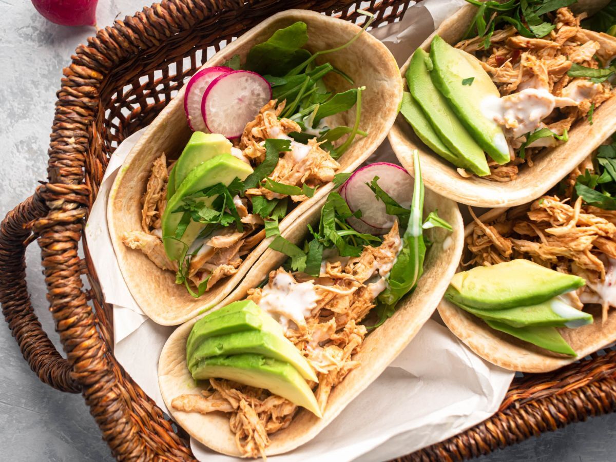 Slow cooker barbacoa chicken shredded and served in corn tortillas with avocado and cilantro.