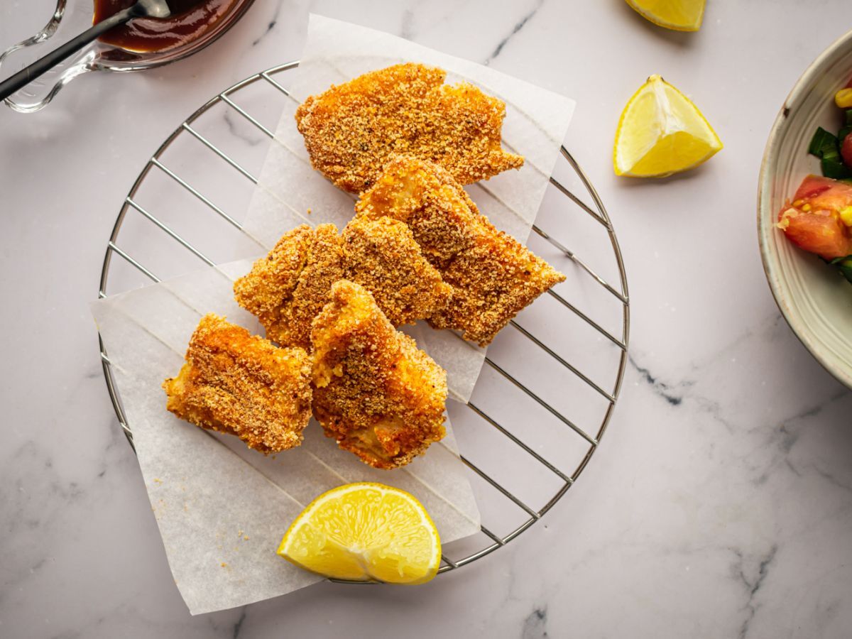 Crispy baked fish with breading on a wire rack with lemons and salad.