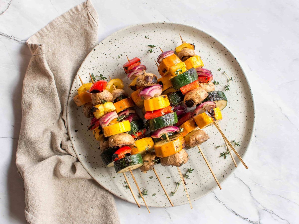 Grilled vegetable skewers seen from above on a beautiful round plate pictured on a marble top table. 