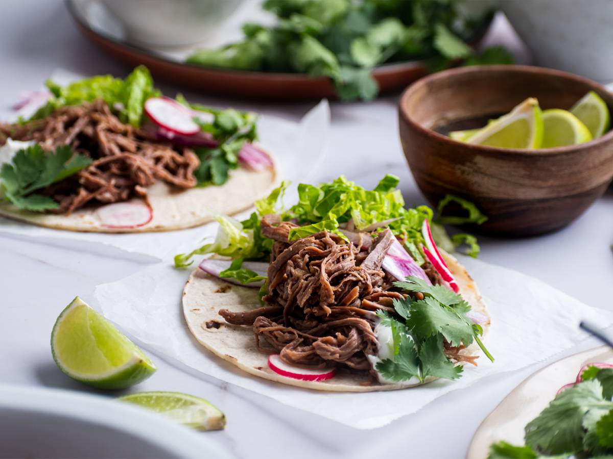 Slow cooker tri tip tacos on white corn tortillas with lettuce, cilantro, and radishes.