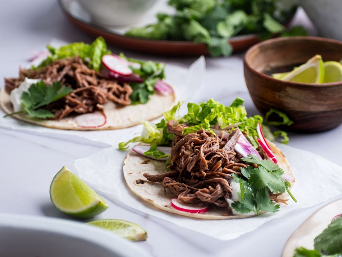 Slow cooker tri tip tacos on white corn tortillas with lettuce, cilantro, and radishes.